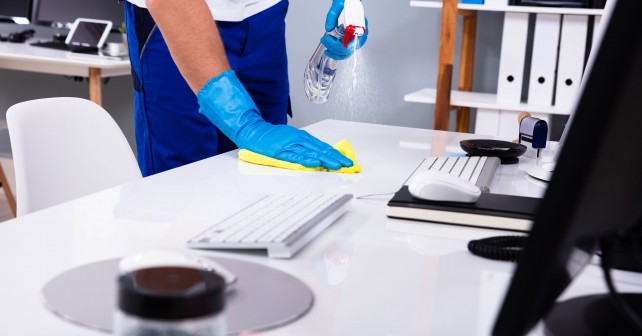 Janitor cleaning white desk in modern office